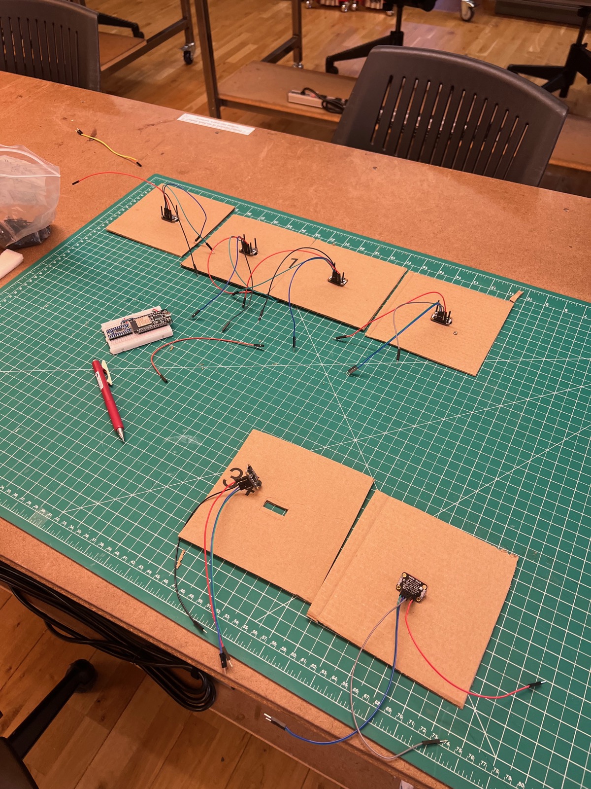 Cardboard panels with photo sensors wired to a microcontroller on a green cutting mat