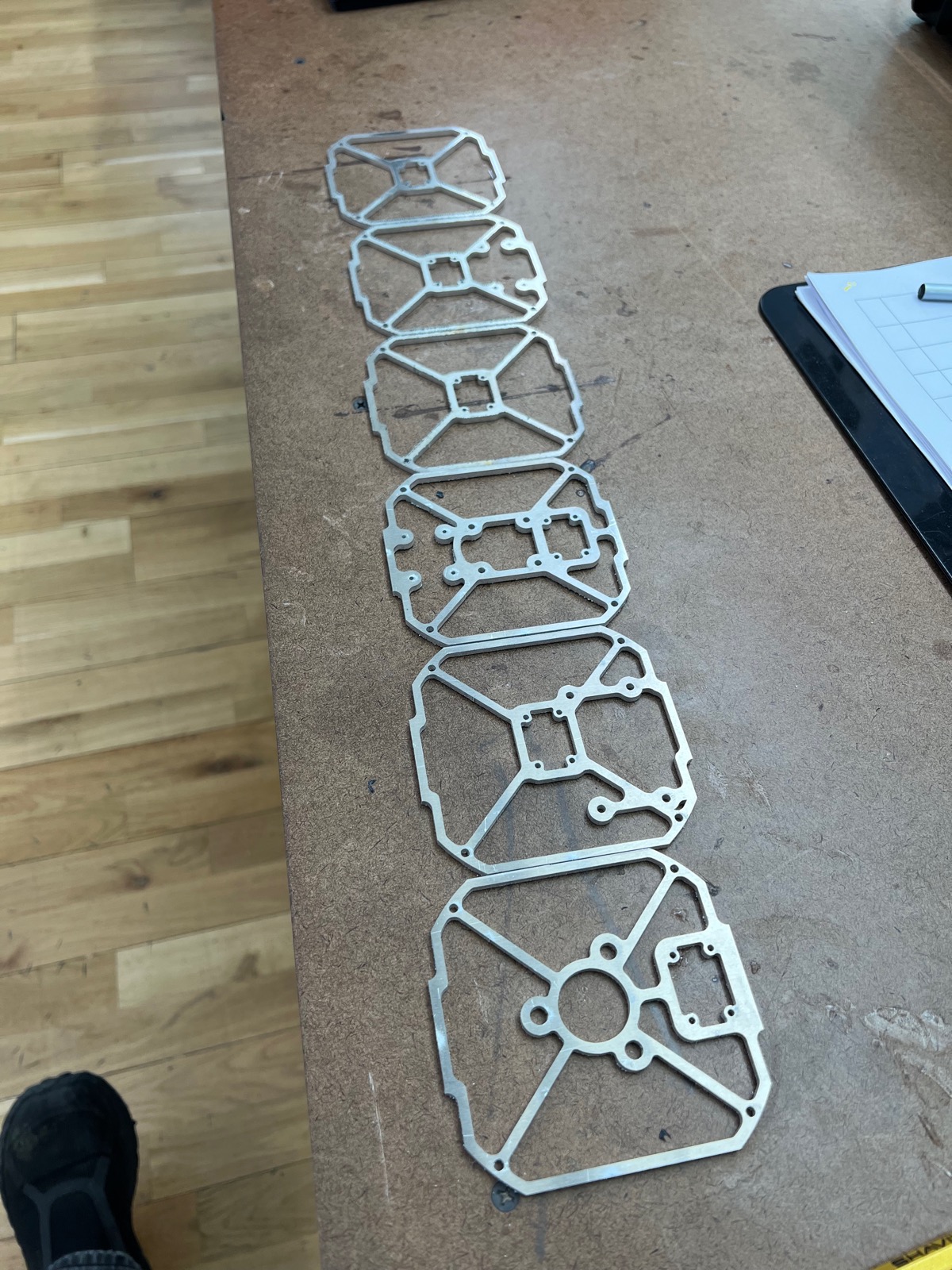 Six laser-cut aluminum cube frame panels laid out in a row on a bench
