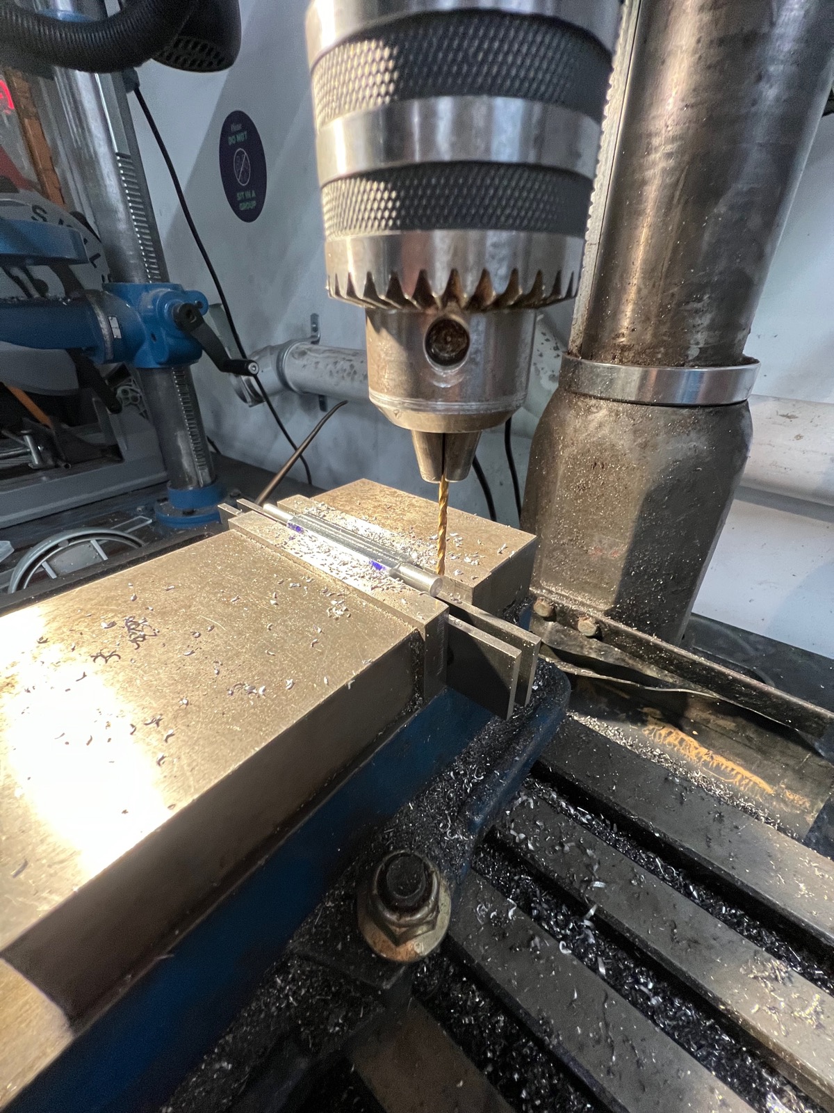 Drill press machining a metal bar held in a vise