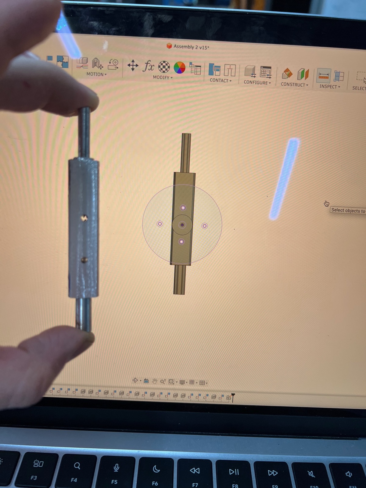 Fusion 360 assembly on a laptop beside a hand-held 3D-printed axle coupler