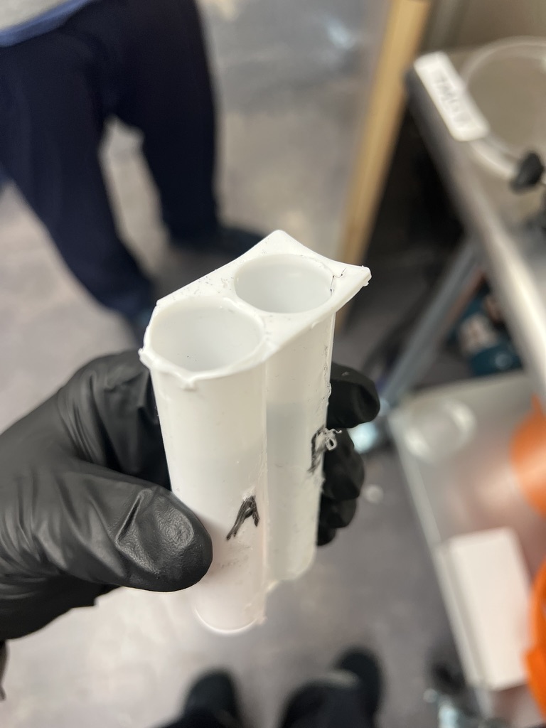 A gloved hand holding an empty white two-barrel silicone cartridge, cracked at the rim