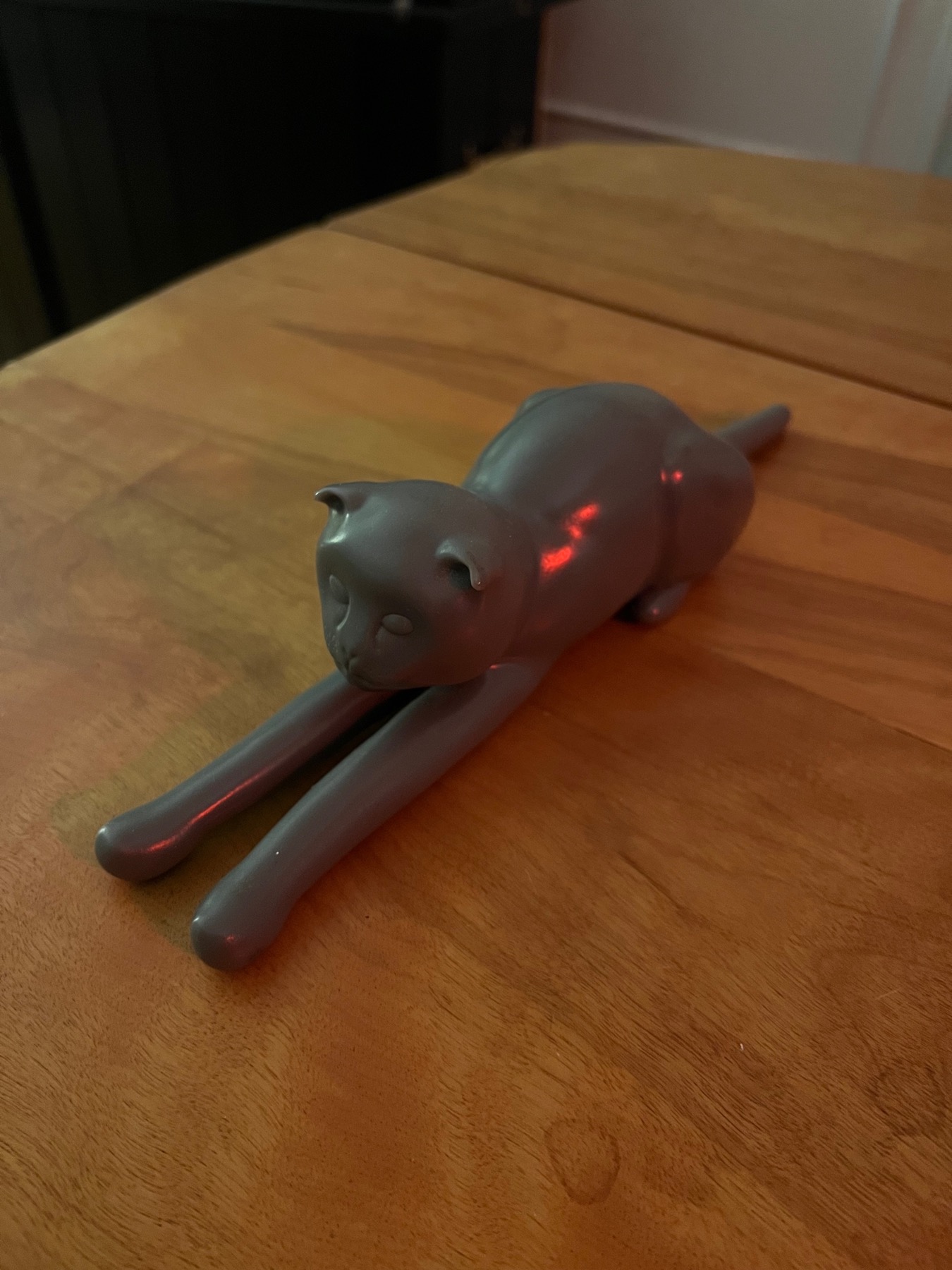 A grey 3D printed cat stretched out low on a wooden table, front legs reaching forward