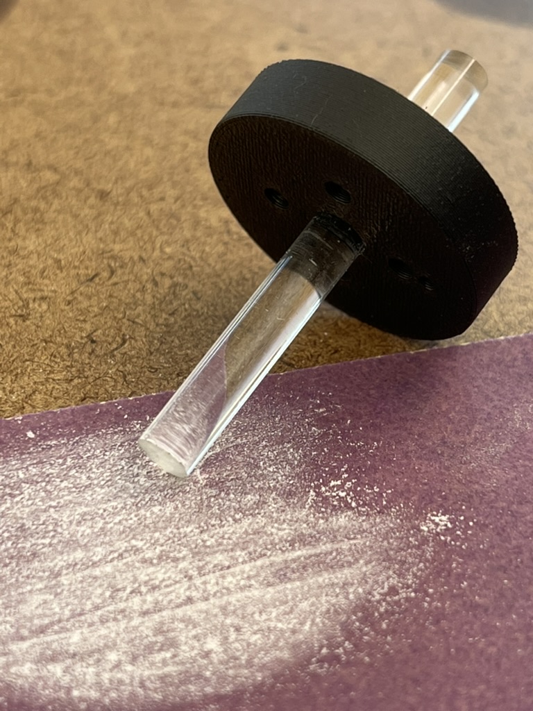 The clear acrylic rod pushed through the black printed rod grab, its cut end resting on purple sandpaper dusted with white acrylic powder.