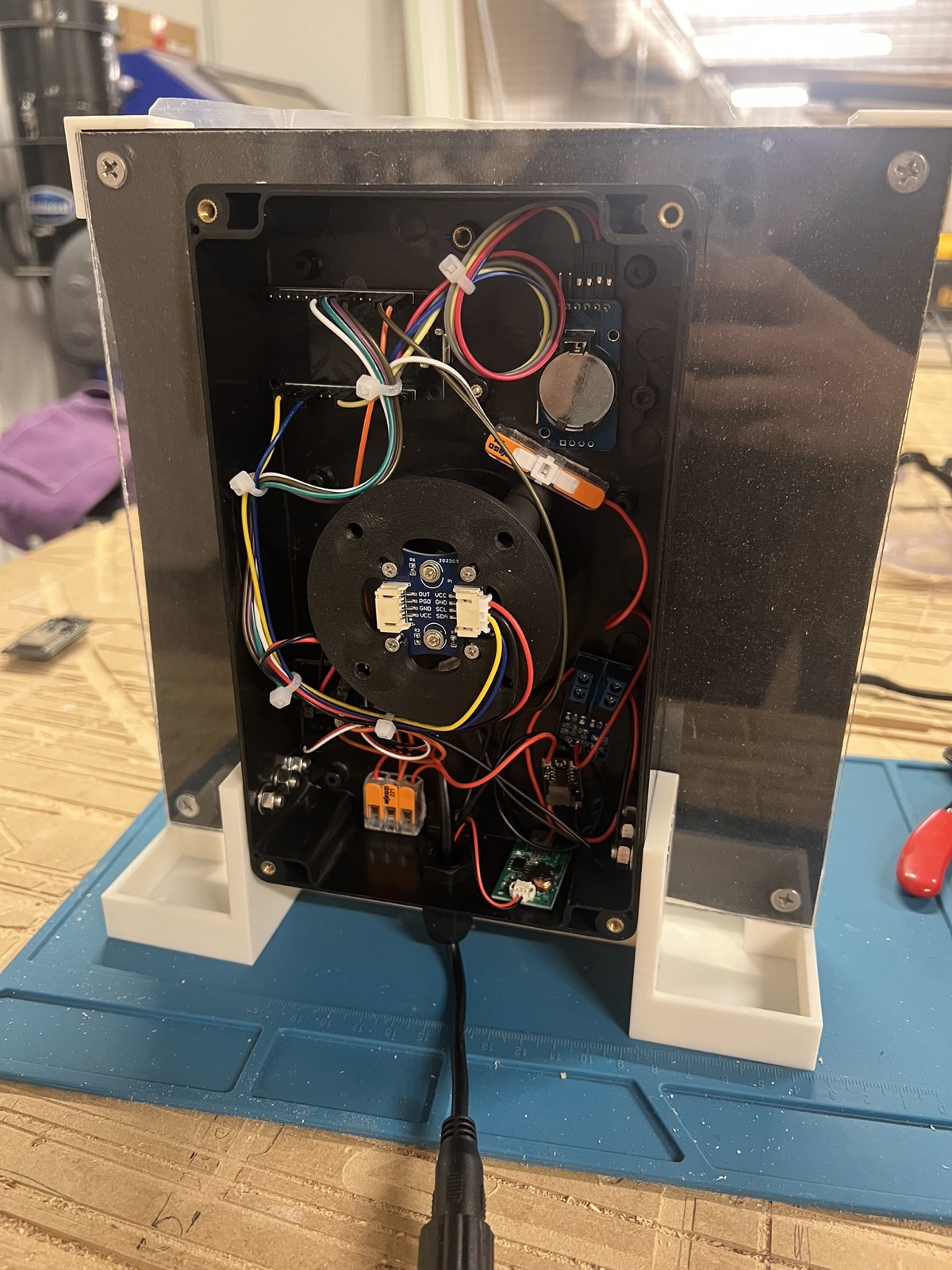 The back of the clock with the enclosure open: the ESP32, a clock module with its coin battery, the encoder on the motor mount, driver boards, lever connectors and a small power board, zip tied together with a black power cable leaving the bottom.