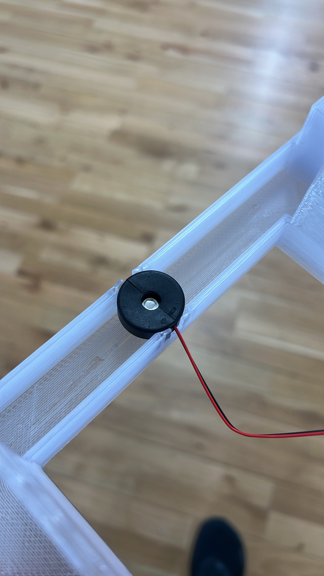 A round black ultrasonic mister sitting in the channel of the translucent printed base tray, its red and black wire running off the edge.