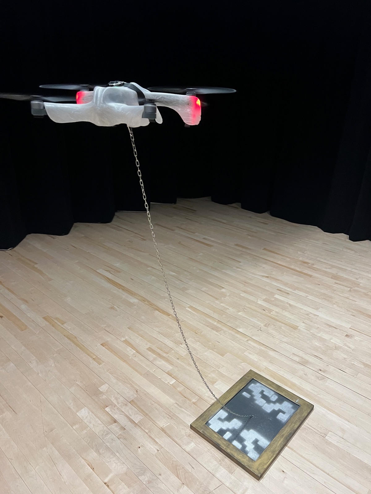 Drone in flight during performance with chain and framed artwork